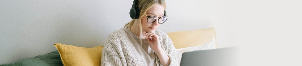 Woman with headphones working or studying with laptop on sofa.
