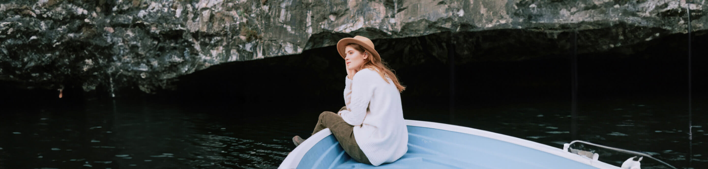 Woman with a hat sitting in a boat looking at a cave.